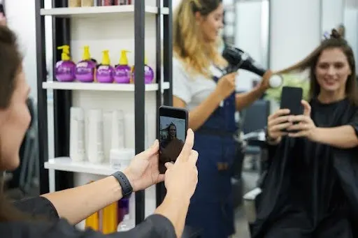 Salon staff capturing a client's blowout on smartphones for social media, showing salon marketing content creation in Dubai.